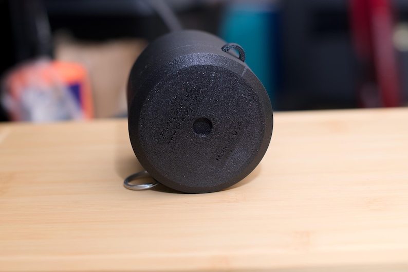 Pode incluir: Uma caneca de cer&acirc;mica preta com uma superf&iacute;cie texturizada, uma pequena al&ccedil;a e um anel de metal preso na parte inferior. A parte inferior da caneca tem o texto "MADE IN USA".