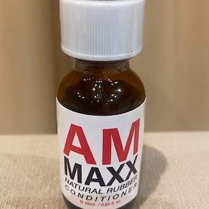May include: A small amber glass bottle with a white cap. The bottle has a white label with red and black text that reads "AM MAXX NATURAL RUBBER CONDITIONER". The bottle contains 25ml / 0.85 fl. oz.