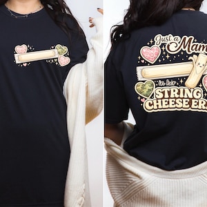 Könnte beinhalten: Schwarzes T-Shirt mit einer Stringkäse-Grafik und dem Text "Just a Mama in her String Cheese Era". Das Design beinhaltet Herzen und Sterne. Das Shirt besteht aus einem weichen, bequemen Material.