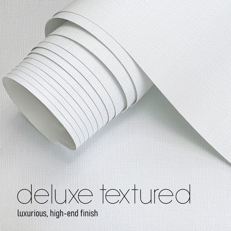 May include: A roll of white, textured wallpaper with a luxurious, high-end finish. The words "deluxe textured" and "luxurious, high-end finish" are printed in black on the wallpaper.