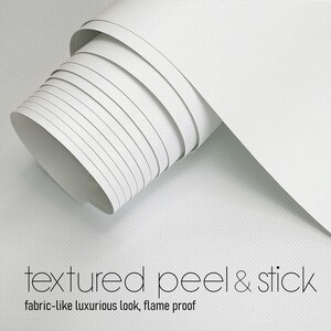 May include: A roll of white, textured peel and stick material. The material is rolled up, revealing the interior and the edge of the roll. The text "textured peel & stick" and "fabric-like luxurious look, flame proof" are visible.