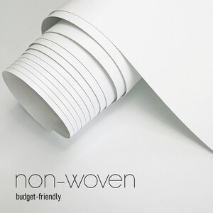 May include: A roll of white non-woven material, partially unrolled, showing layers of the paper. The text "non-woven" and "budget-friendly" are displayed in a minimalist font at the bottom of the image.
