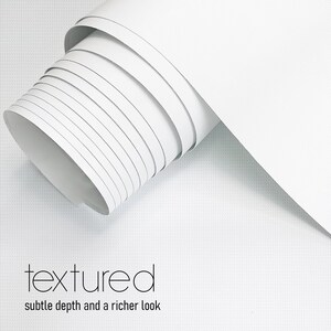 May include: A roll of white textured material with subtle depth and a richer look. The material is tightly rolled, revealing the edges of each layer. The word "textured" is displayed in a modern font.