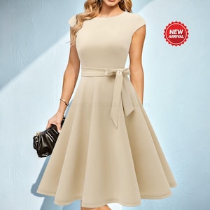May include: A beige cap-sleeve dress with a belted waist and a flared skirt. The dress features a bow detail at the waist and a "NEW ARRIVAL" sticker. A black clutch is held in the left hand.