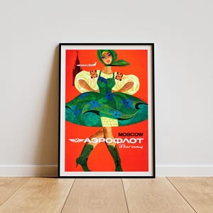 Könnte beinhalten: Gerahmtes Vintage-Reiseposter für Aeroflot. Es zeigt eine Frau in grünem Kleid und Kopftuch vor rotem Hintergrund. Der Text "Moskau" und das Aeroflot-Logo sind abgebildet, ebenso wie ein Flugzeug und ein Gebäude.