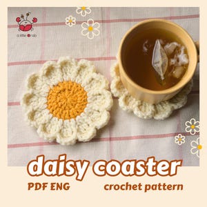 May include: Two daisy-shaped crochet coasters, one holding a mug of tea. The coasters are white with yellow centers. The image includes the text "daisy coaster" and "crochet pattern".