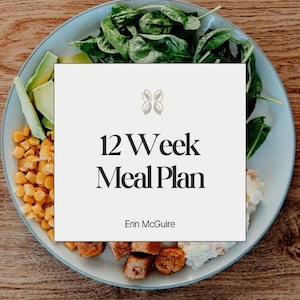 May include: A plate of food with avocado, corn, spinach, and cooked meat. A card in the centre reads "12 Week Meal Plan" by Erin McGuire. The plate is light blue, and the background is a wooden surface.