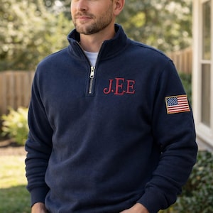 May include: Navy blue pullover sweatshirt with a quarter-zip collar and the embroidered initials "J.E.E" in red. An American flag patch is on the left sleeve. The sweatshirt is made of a soft material.