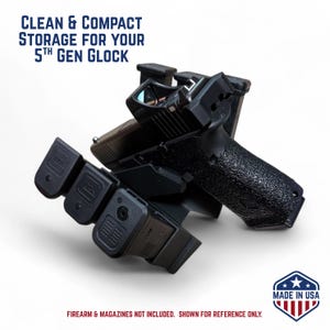 Könnte beinhalten: Schwarzer Aufbewahrungsständer für eine 5. Generation Glock, der eine Handfeuerwaffe und Magazine hält. Der Ständer ist schwarz und trägt den Text "CLEAN & COMPACT STORAGE FOR YOUR 5TH GEN GLOCK" und "MADE IN USA". Feuerwaffe und Magazine sind nicht enthalten.