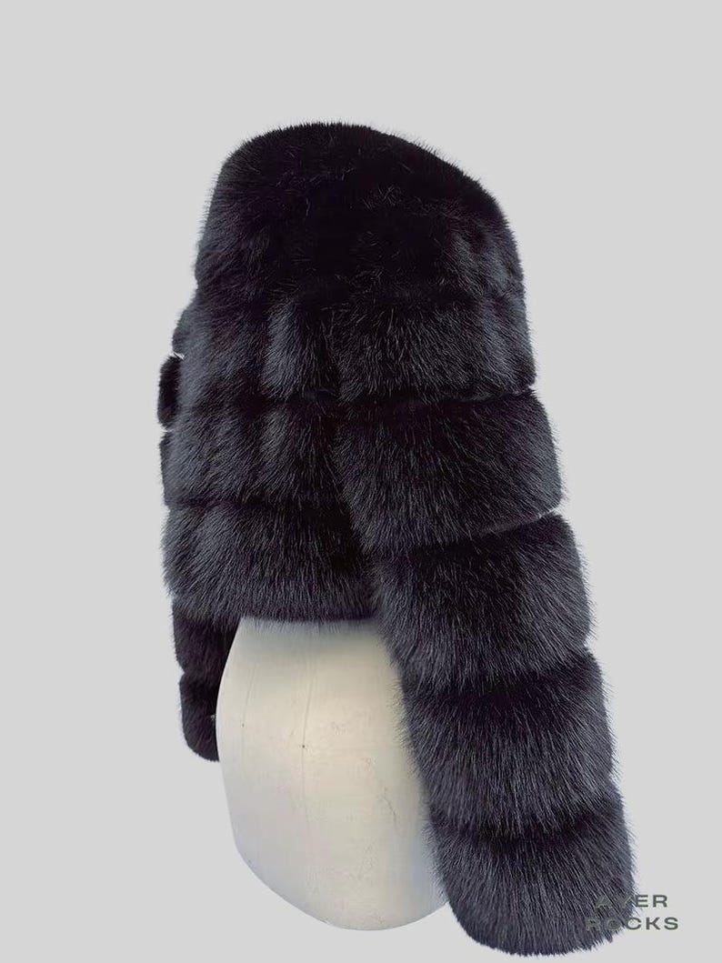 May include: A black fur bolero jacket. The cropped jacket is displayed on a white mannequin. The fur is layered horizontally, creating a textured appearance. The sleeves are long and the jacket is a solid black colour.
