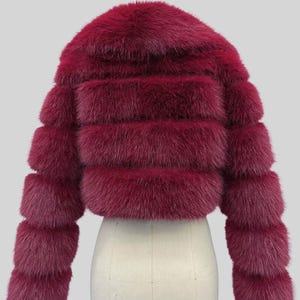 May include: A burgundy fur jacket with a round collar and horizontal fur bands. The sleeves are long and also feature horizontal bands. The jacket is displayed on a white mannequin. The text "AYER ROCKS" is visible in the bottom right corner.