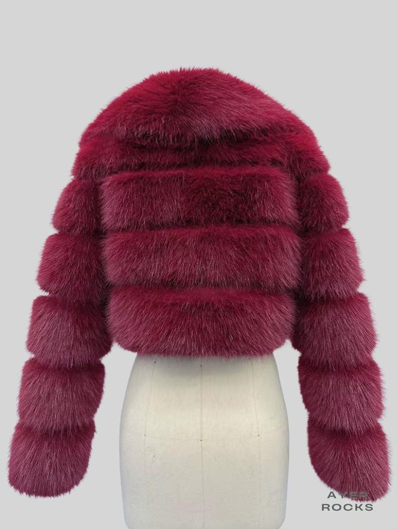 May include: A burgundy fur jacket with a round collar and horizontal fur bands. The sleeves are long and also feature horizontal bands. The jacket is displayed on a white mannequin. The text "AYER ROCKS" is visible in the bottom right corner.