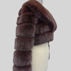 May include: A brown fur jacket with a cropped design. The jacket features horizontal bands of fur, creating a textured appearance. The sleeves are long and the jacket is displayed on a mannequin.