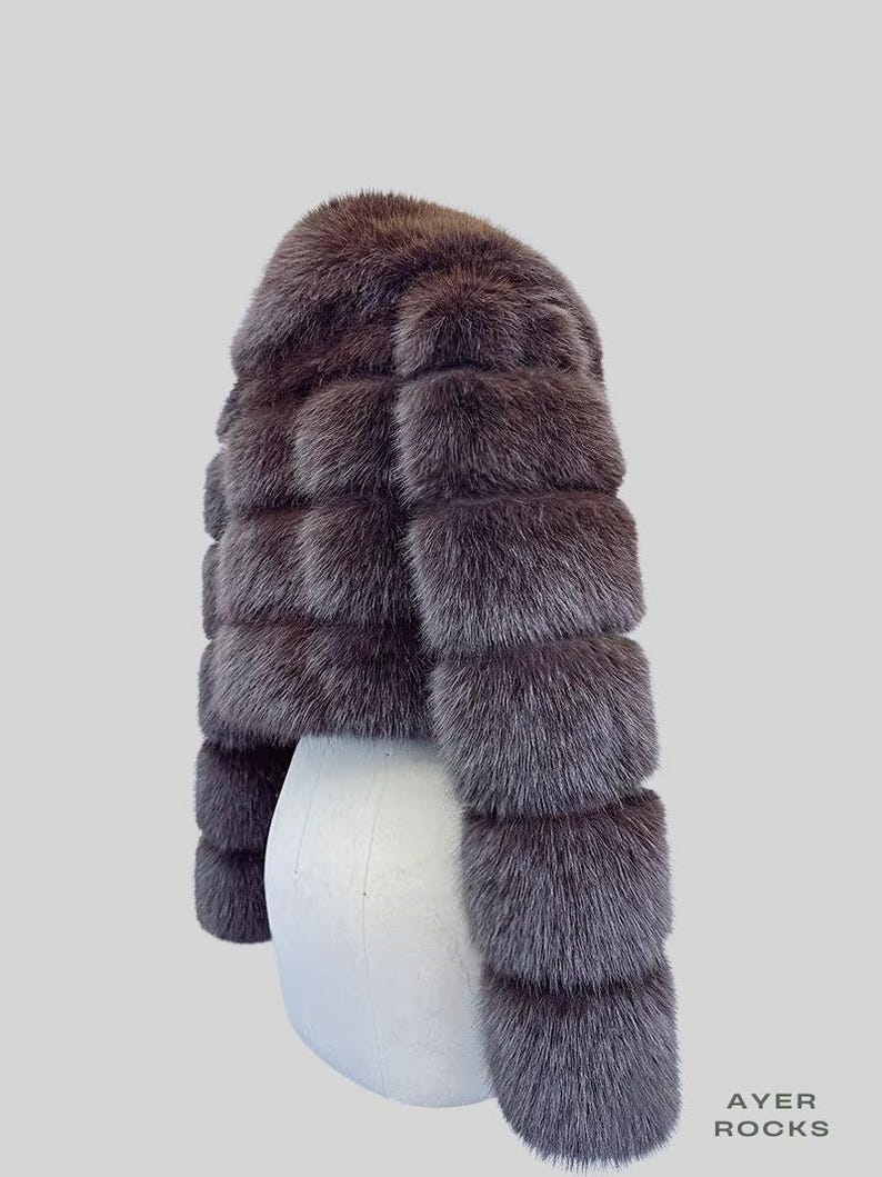 May include: A short, brown fur jacket with a rounded neckline and horizontal fur panels. The jacket is displayed on a white mannequin. The text "AYER ROCKS" is visible in the lower right corner.
