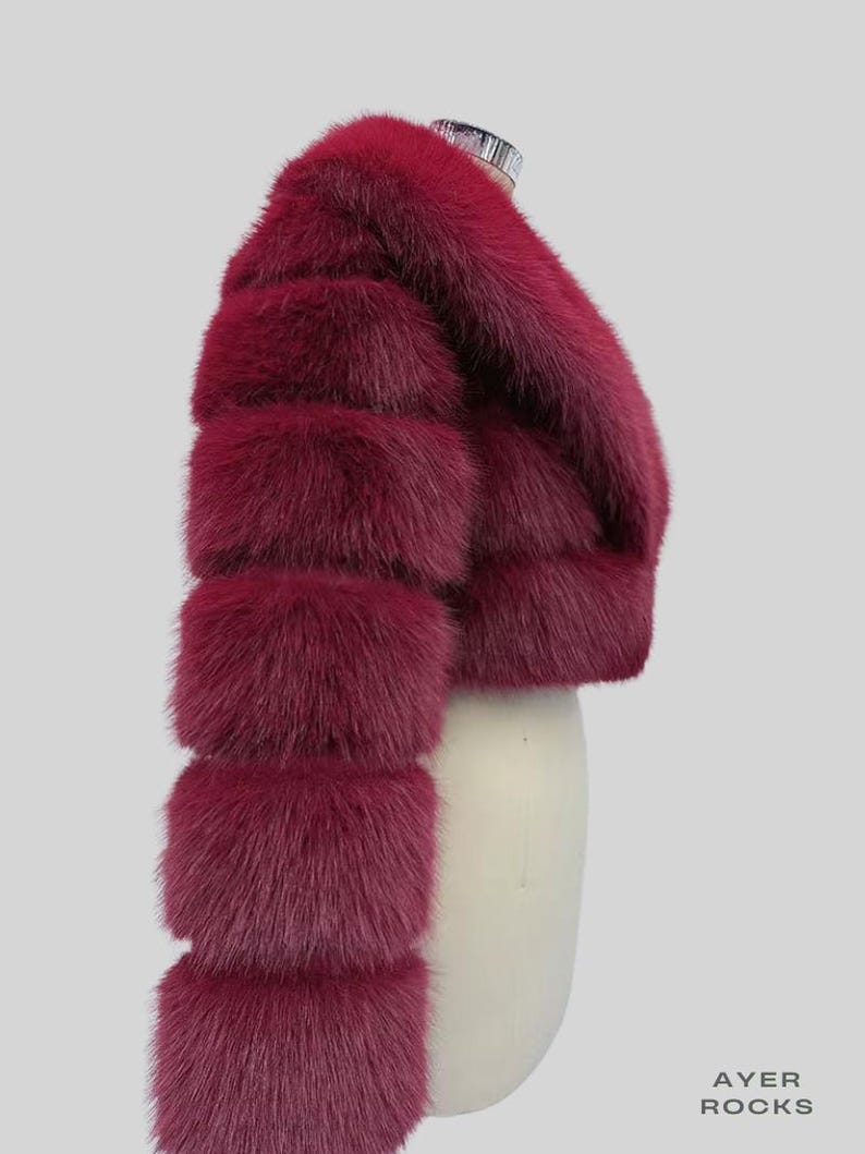 May include: A deep burgundy fur bolero jacket with a cropped design. The jacket has horizontal fur bands on the sleeves and a rounded neckline. The fur looks soft and plush, with a slight sheen. The jacket is displayed on a mannequin.