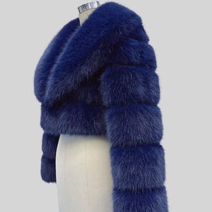 May include: A navy blue faux fur cropped jacket. The jacket has a wide collar and sleeves with horizontal bands. It is displayed on a mannequin against a light grey background. The text "AYER ROCKS" is visible in the lower right corner.