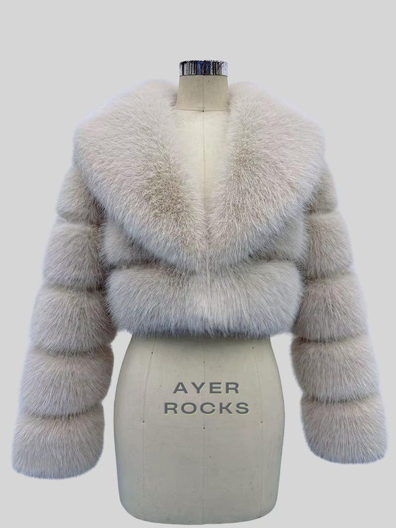 May include: A light grey faux fur jacket, cropped in length, with a broad collar and horizontally banded sleeves. The jacket is displayed on a dress form, with the text "AYER ROCKS" visible. The design and texture suggest a focus on outerwear fashion.
