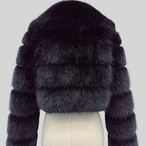 May include: A black fur jacket with a cropped design. The jacket has horizontal bands of fur and long sleeves. The garment is displayed on a mannequin against a light grey background.