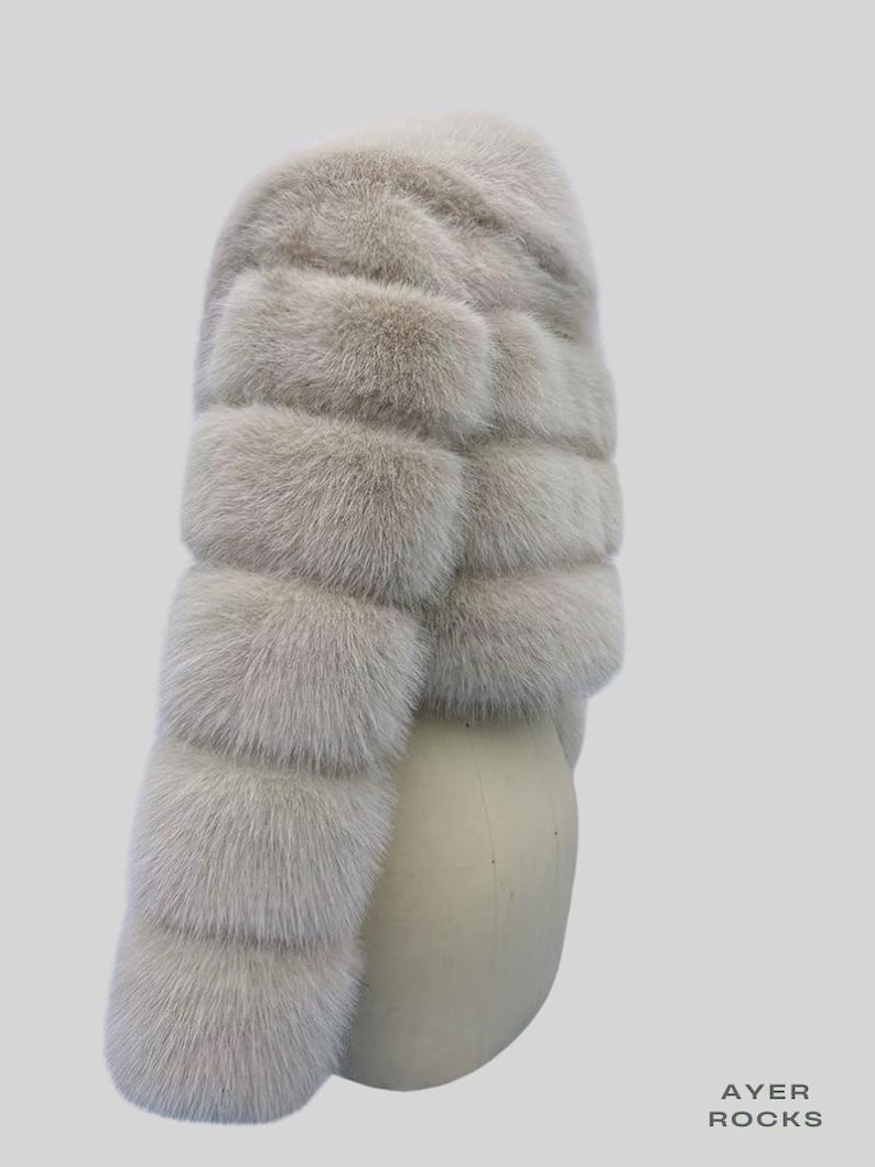 May include: A light grey fur scarf with a layered design. The scarf is made of soft, fluffy fur and is displayed on a mannequin head against a light grey background. The text "AYER ROCKS" is visible in the bottom right corner.