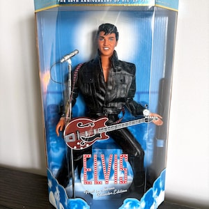 Könnte beinhalten: Elvis Presley Sammleredition-Puppe in einer transparenten Vitrine. Die Puppe trägt eine schwarze Lederjacke und -hose und hält eine rotbraune Gitarre. Die Verpackung enthält den Text "The Elvis Presley Collection" und "First in a Series Collector Edition."