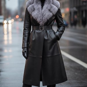 May include: A long black leather coat with a gray fur collar and a matching belt. The coat features a classic design with a tailored fit, long sleeves, and a knee-length hem. The model is wearing black gloves and boots.