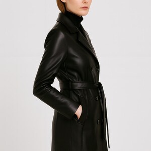 May include: A black leather trench coat with a double-breasted design and a matching belt. The coat features a classic collar, long sleeves, and pockets. The model is wearing a black turtleneck.