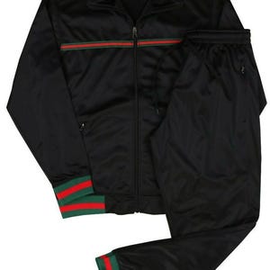 Könnte beinhalten: Schwarzer Trainingsanzug mit passender Jacke und Hose. Die Jacke hat einen Reißverschluss und einen grünen und roten Streifen über der Brust. Bündchen und Knöchel haben grüne und rote Streifen.