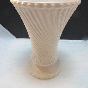 May include: A cream-colored ceramic vase with a flared top and a round base. The vase has a spiral design on the body and a beaded rim. The vase is approximately 8 inches tall.
