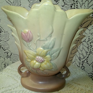 May include: A vintage ceramic vase in a soft, muted color palette. The vase features a flared, petal-like rim and is adorned with embossed floral designs, including a large yellow flower and a pink tulip. The base is a darker shade of brown.