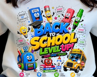 May include: A white sweatshirt featuring a colorful graphic with the text BACK TO SCHOOL LEVEL UP! surrounded by cartoon school supplies including a blue notebook, yellow pencil, pink eraser, green marker, blue backpack, red apple, and yellow school bus.