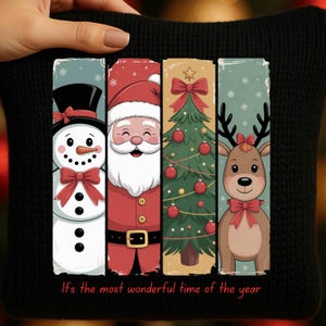 Peut inclure: Coussin noir avec quatre panneaux verticaux illustrant des motifs de Noël. On y voit un bonhomme de neige, le Père Noël, un sapin de Noël et un renne, tous avec des détails rouges. Le texte "It's the most wonderful time of the year" est imprimé en bas.