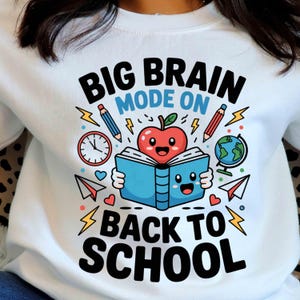 Könnte beinhalten: Weißes Sweatshirt mit farbenfrohem Grafikdesign. Das Design zeigt den Text "BIG BRAIN MODE ON BACK TO SCHOOL" mit Illustrationen eines Apfels, eines Buches, Bleistiften, eines Globus und einer Uhr.
