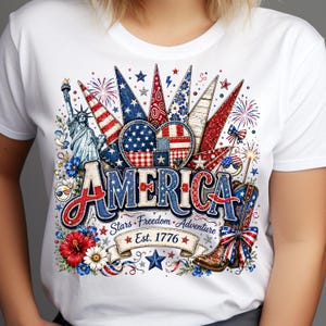 Peut inclure: Un t-shirt blanc avec une impression graphique représentant la Statue de la Liberté, un drapeau américain en forme de cœur, une botte de cow-boy et des feux d'artifice. Le texte indique AMERICA, Stars, Freedom, Adventure et Est. 1776.