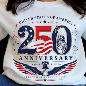 May include: A white sweatshirt featuring a graphic with the text UNITED STATES OF AMERICA 250TH ANNIVERSARY. The design includes the number 250 with stars and stripes, the Statue of Liberty, the Liberty Bell, an eagle, and the years 1776 and 2026.