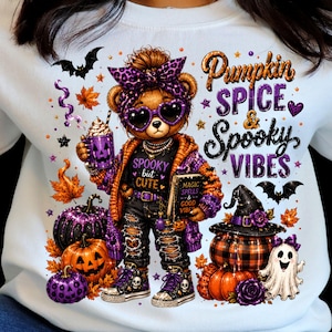 Peut inclure: Un sweat-shirt blanc avec une illustration d'ours en peluche portant un bandeau léopard violet et des lunettes en forme de cœur. L'ours tient un mug citrouille et un livre intitulé Magic Spells & Good Vibes. Le texte indique Pumpkin Spice & Spooky Vibes.