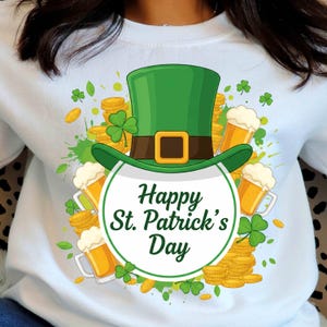 Peut inclure: Sweat-shirt blanc avec un motif de la Saint-Patrick. Le motif représente un chapeau de lutin vert avec une boucle dorée, des pièces d'or, des trèfles et des chopes de bière. Le texte "Happy St. Patrick's Day" est en vert.