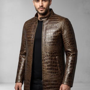 May include: A brown, long leather coat with a crocodile skin texture. The coat has a stand-up collar, a front zipper, and two side pockets. The coat is a medium length, reaching to the mid-thigh.