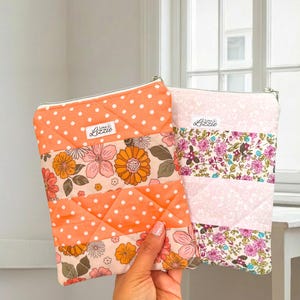 May include: Two quilted pouches with zip closures. One is orange with white polka dots and floral patterns. The other is pink with floral patterns. Both have the "Love & Lizzie" logo.