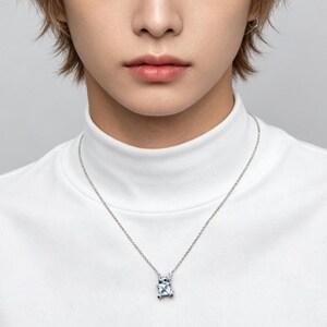 May include: A silver necklace with a pendant featuring a blue and white design. The pendant is suspended from a delicate chain. The person in the image is wearing a white turtleneck.