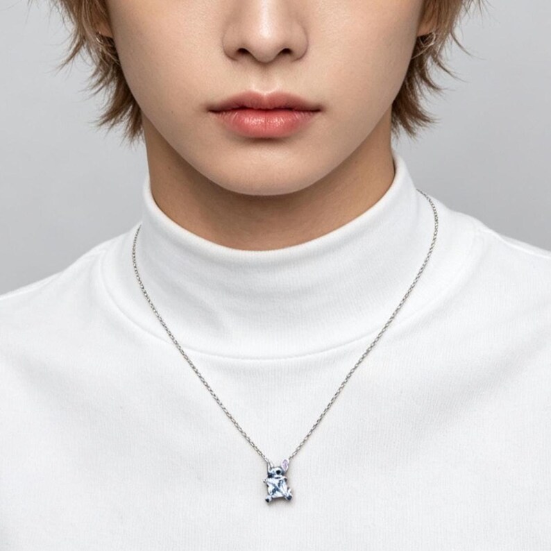May include: A silver necklace with a pendant featuring a blue and white design. The pendant is suspended from a delicate chain. The person in the image is wearing a white turtleneck.