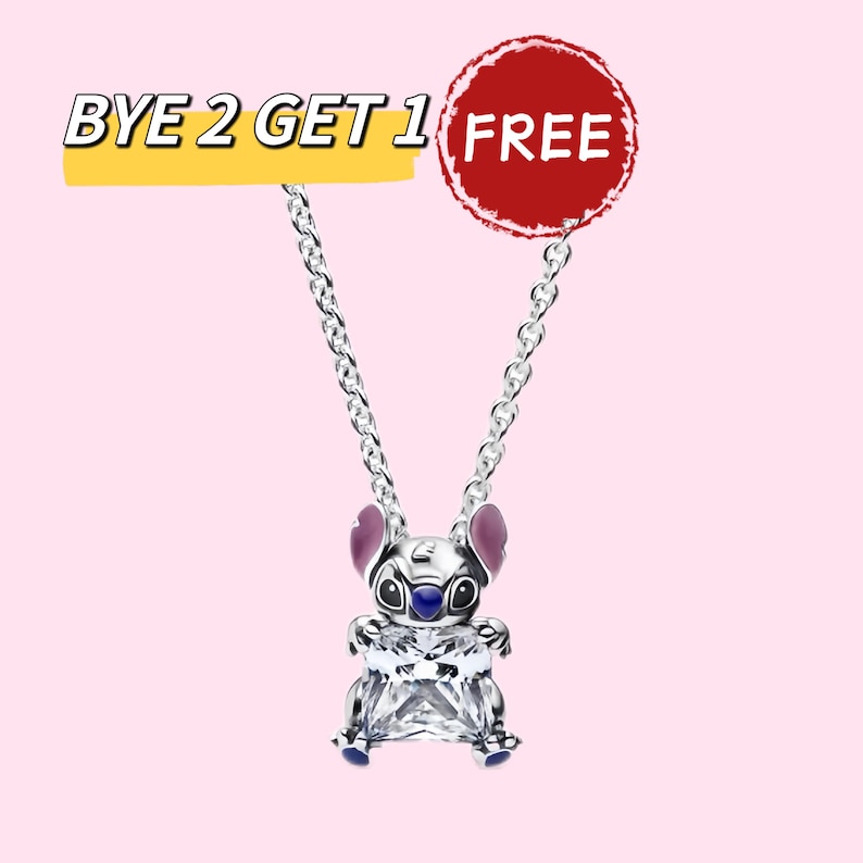 May include: A silver-colored necklace featuring a charm shaped like a cartoon character with purple ears and blue accents. The charm has a large, clear, square-cut crystal. The image also includes the text "BYE 2 GET 1 FREE" on a yellow banner and a red circle with the word "FREE".