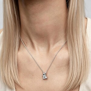 May include: A silver necklace with a square, clear gemstone pendant. The pendant is set in a silver frame and hangs from a delicate silver chain. The necklace is worn around the neck.