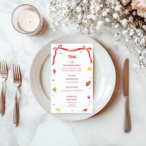 May include: A white plate with a menu card, silverware, and a lit candle. The menu card has a red ribbon design and lists food items. The scene is decorated with flowers and set on a marble surface.