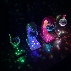 Puede incluir: Cuatro l&aacute;mparas de bola de discoteca con bases y arcos de colores. Las bolas de discoteca espejadas reflejan la luz. Las bases son blancas, rosas y negras. Los arcos coinciden con el color de la base. Luces de colores.