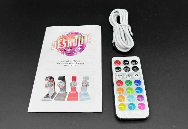 Puede incluir: Un conjunto de altavoz de discoteca multicolor con un mando a distancia, un manual de instrucciones y un cable USB blanco. El manual de instrucciones presenta el texto "DESKOLITE" y "Multi-Color Disco Speaker". El mando tiene botones.