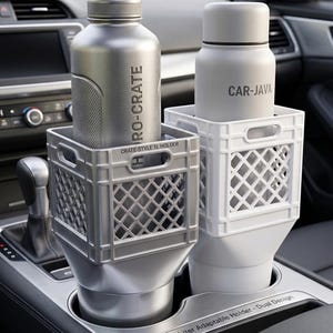 May include: A silver water bottle and a white coffee tumbler sit in a car's center console. Both are in crate-style holders. The water bottle is labeled "H2O-CRATE" and the coffee tumbler is labeled "CAR-JAVA". The console reads "1-Liter Adaptable Holder - Dual Design".