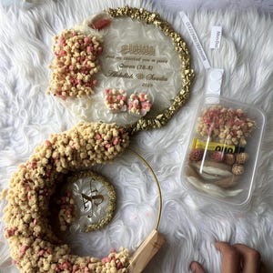 K&ouml;nnte beinhalten: Dekorative Hochzeits- oder Event-Dekoration mit klarer Acrylbasis, goldenen Verzierungen und floralen Akzenten in Rosa und Beige. Das Design umfasst ein rundes Element mit Text und eine spiralf&ouml;rmige Form. Der Text lautet "And we created you in pairs Quran (78.8) Abdullah @ Saadia 2020."