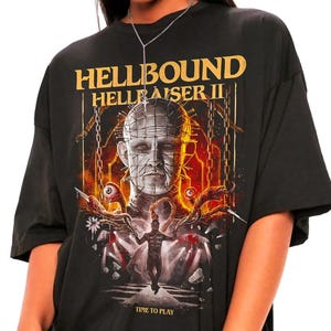 May include: Black Hellbound Hellraiser II graphic t-shirt. The shirt features a detailed illustration of a character from the horror film, with the text "TIME TO PLAY" at the bottom. The design is in shades of red, white, and grey.