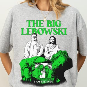Könnte beinhalten: Graues T-Shirt mit einem grünen Grafikdesign aus dem Film "The Big Lebowski". Die Grafik zeigt den Text "THE BIG LEBOWSKI" über einem Bild von zwei Männern und den Text "I AM THE DUDE" darunter.
