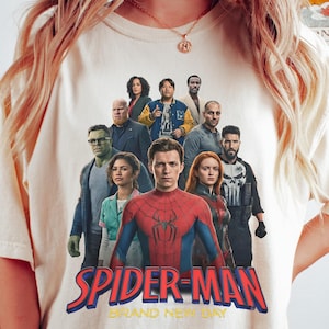Op de afbeelding: Ivoor Comfort Colors T-shirt met een afbeelding van Spider-Man en andere personages. De tekst "SPIDER-MAN BRAND NEW DAY" is in rood en blauw. Het shirt heeft een ronde hals.